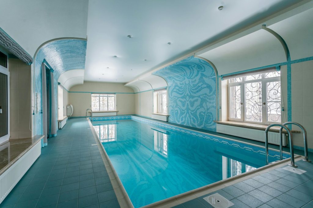 Amplia piscina cubierta con hermoso diseño de azulejos azules e iluminación natural.