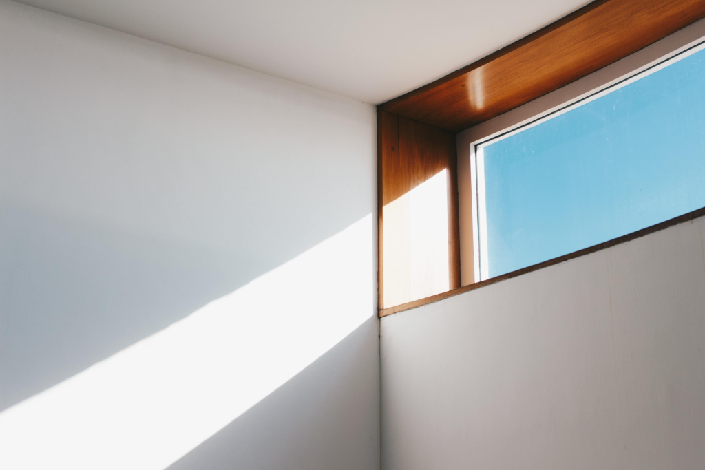 Un interior minimalista que muestra la luz del sol entrando a través de una moderna ventana de vidrio contra un cielo azul.